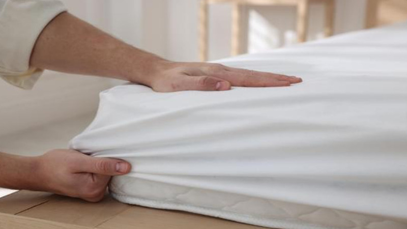 Hands pulling a white fitted sheet over a mattress corner